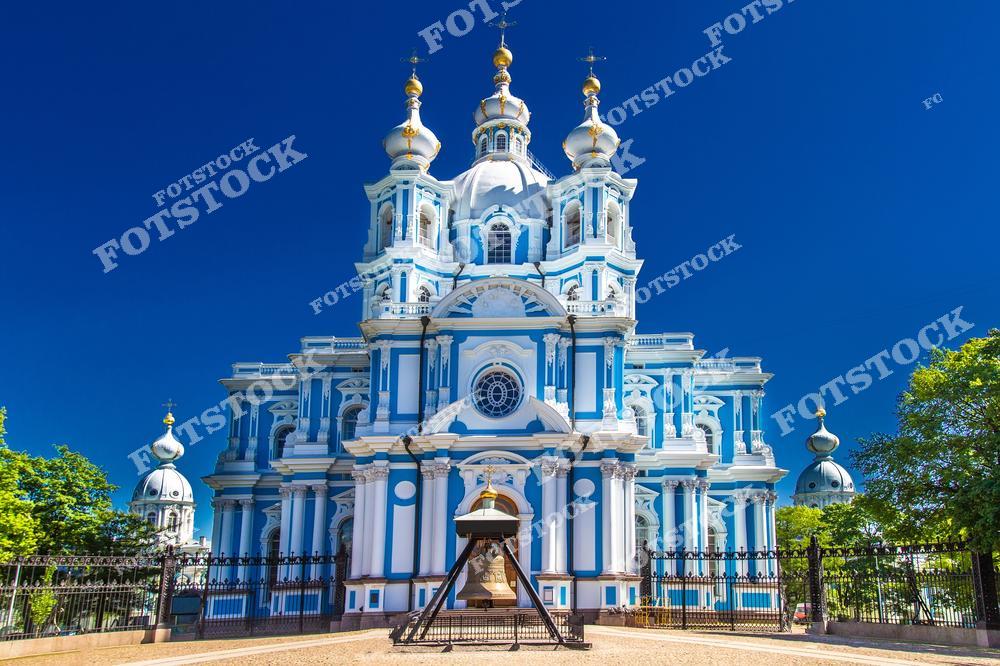 На этом фото представлен Смольный собор в Санкт-Петербурге с видом на городскую набережную. Храм на фоне чистого голубого неба подчеркивает красоту архитектуры северной столицы России. Снимок отражает величие исторических зданий, гармонию с окружающей городской средой и культурное наследие Петербурга. Фотография идеально подходит для туристических публикаций, коллекций фотографий северной столицы, музейных путеводителей и постеров, демонстрируя архитектурное богатство и атмосферу города.